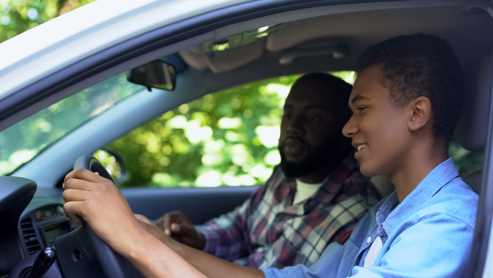 Caring parent teaching son how to drive car