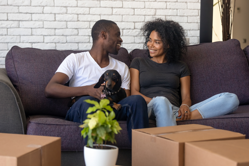 happy african american couple in new rented home with boxes and dog