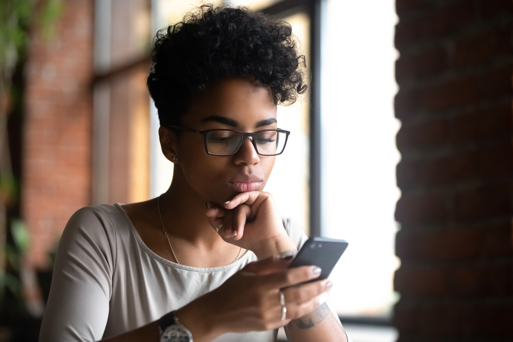 serious african american woman looking at phone for cheap car insurance in arizona