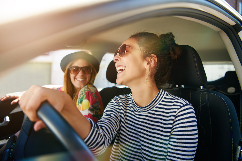 Smiling happy young woman giving her friend a lift in her car in town
