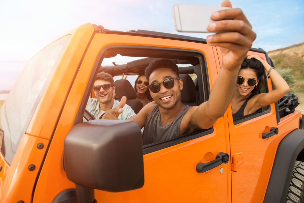 Group of happy young friends taking a selfie while sitting in a convertible car outdoors