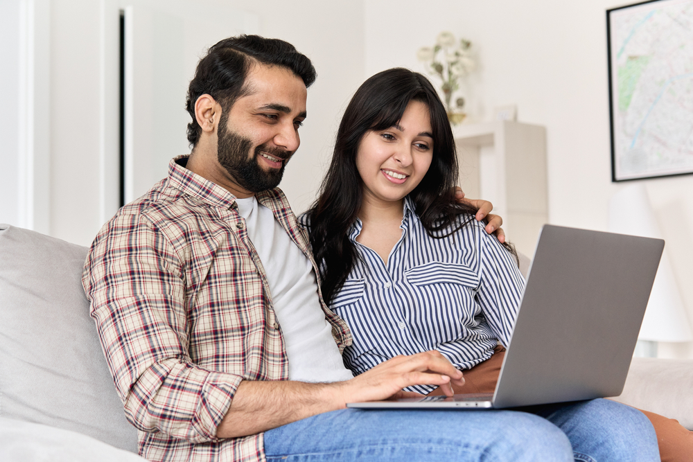 young couple researching life insurance on laptop sitting on couch