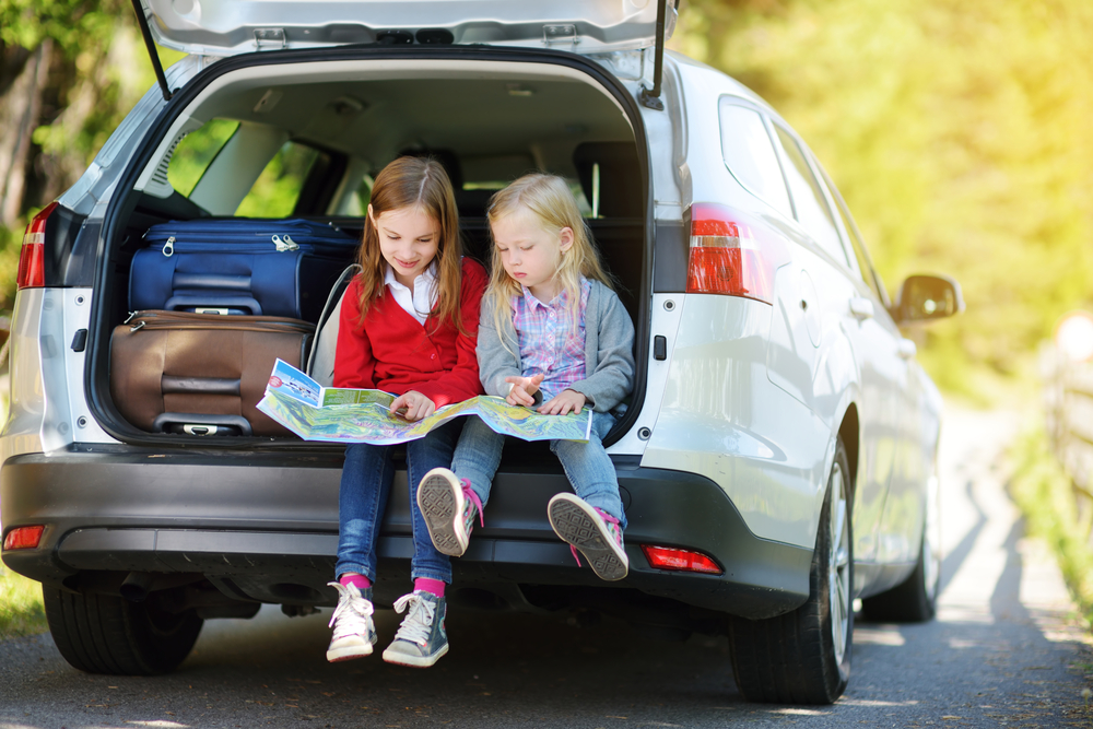 young children sitting on back of car with map in hand