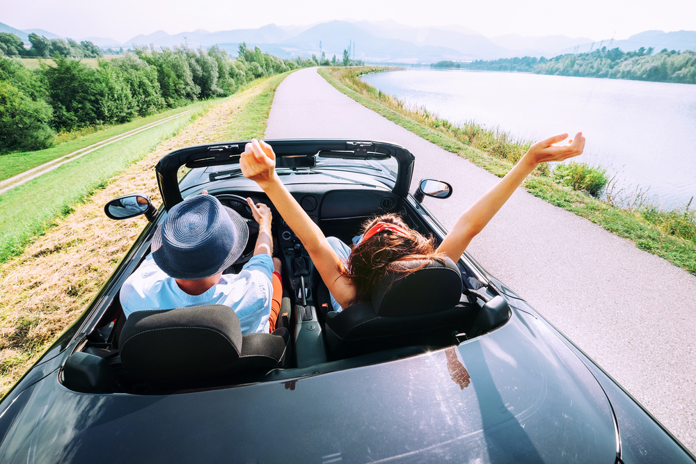 couple in convertible driving down road on vacation