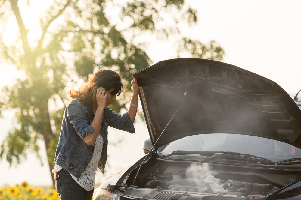 woman standing next to car with hood up as its overheating