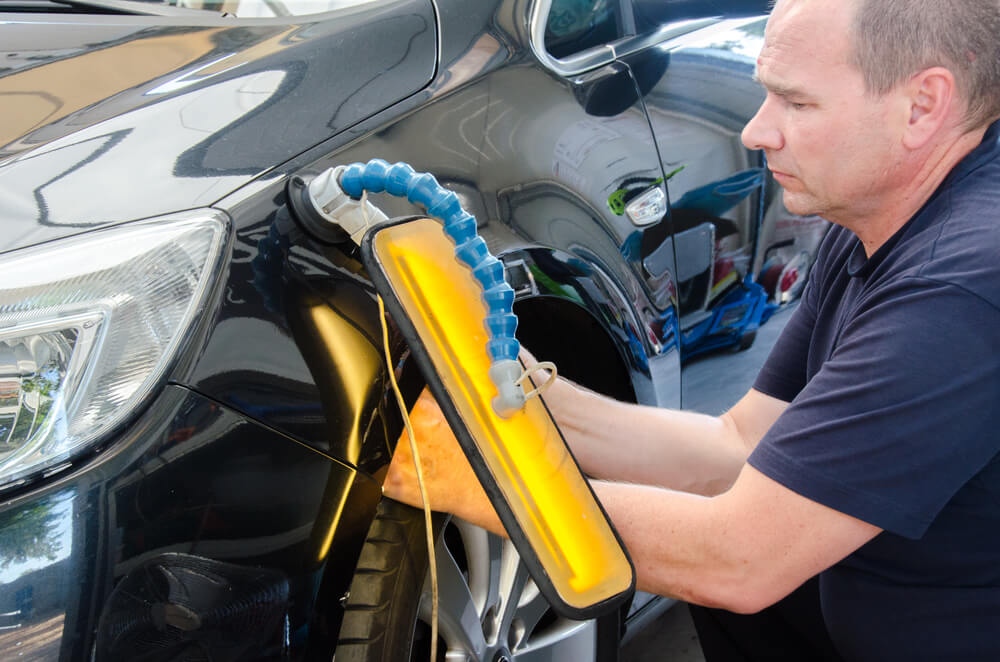 Technician in car service with tools for repairing dents in car body